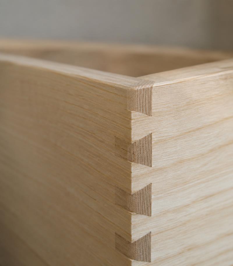 Close view of crisp hand-cut dovetail pins joining two pale ash boards