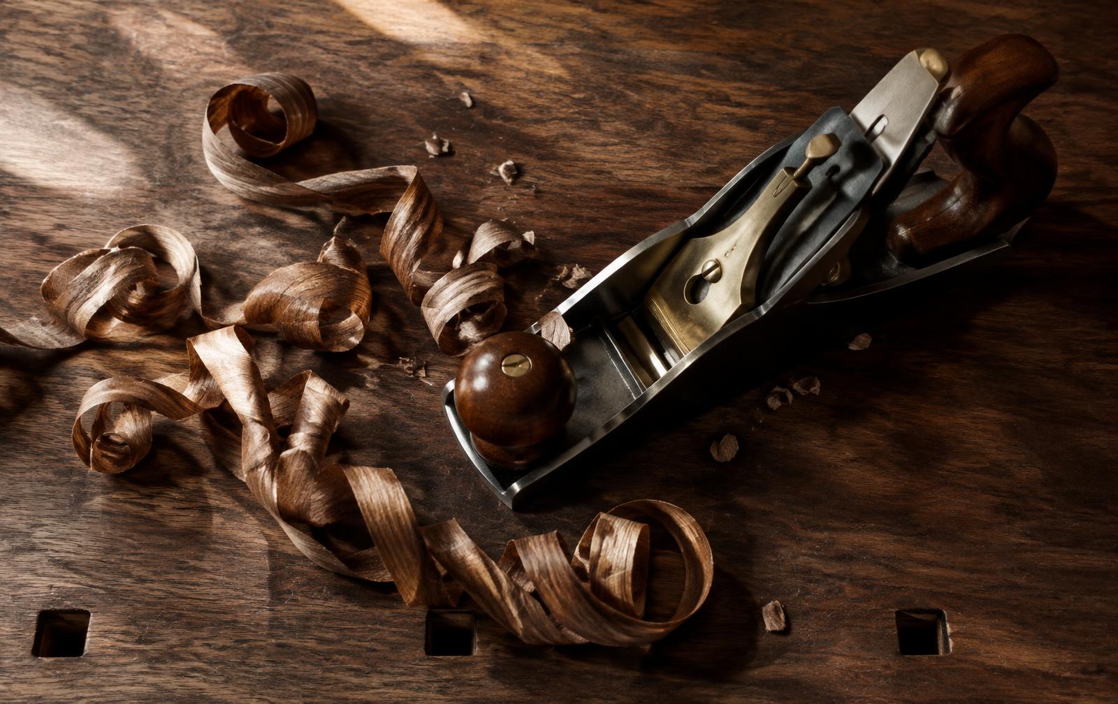 A brass and steel hand plane resting among curled walnut shavings on a traditional workbench